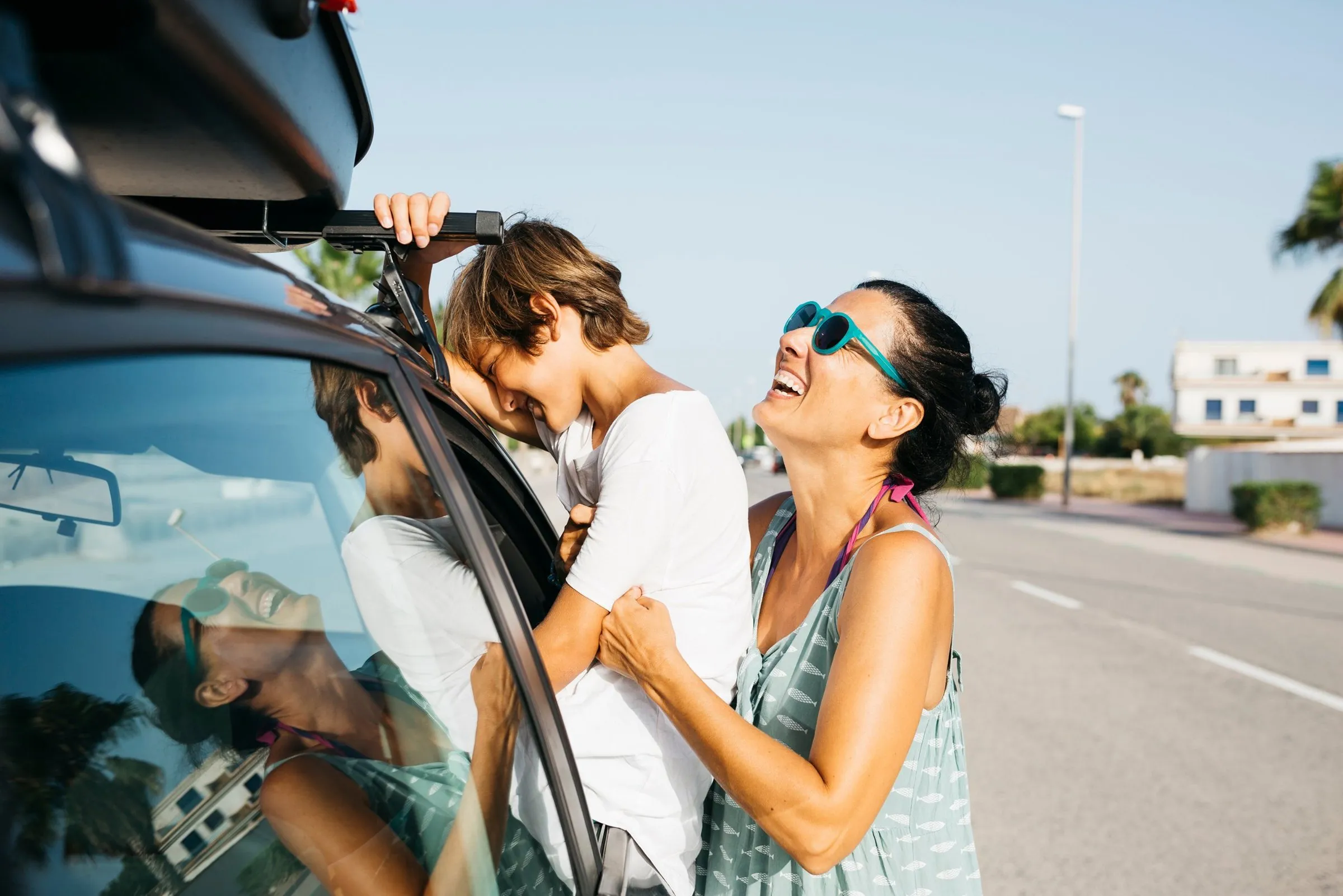 A parent and child laughing beside a car with a roof box