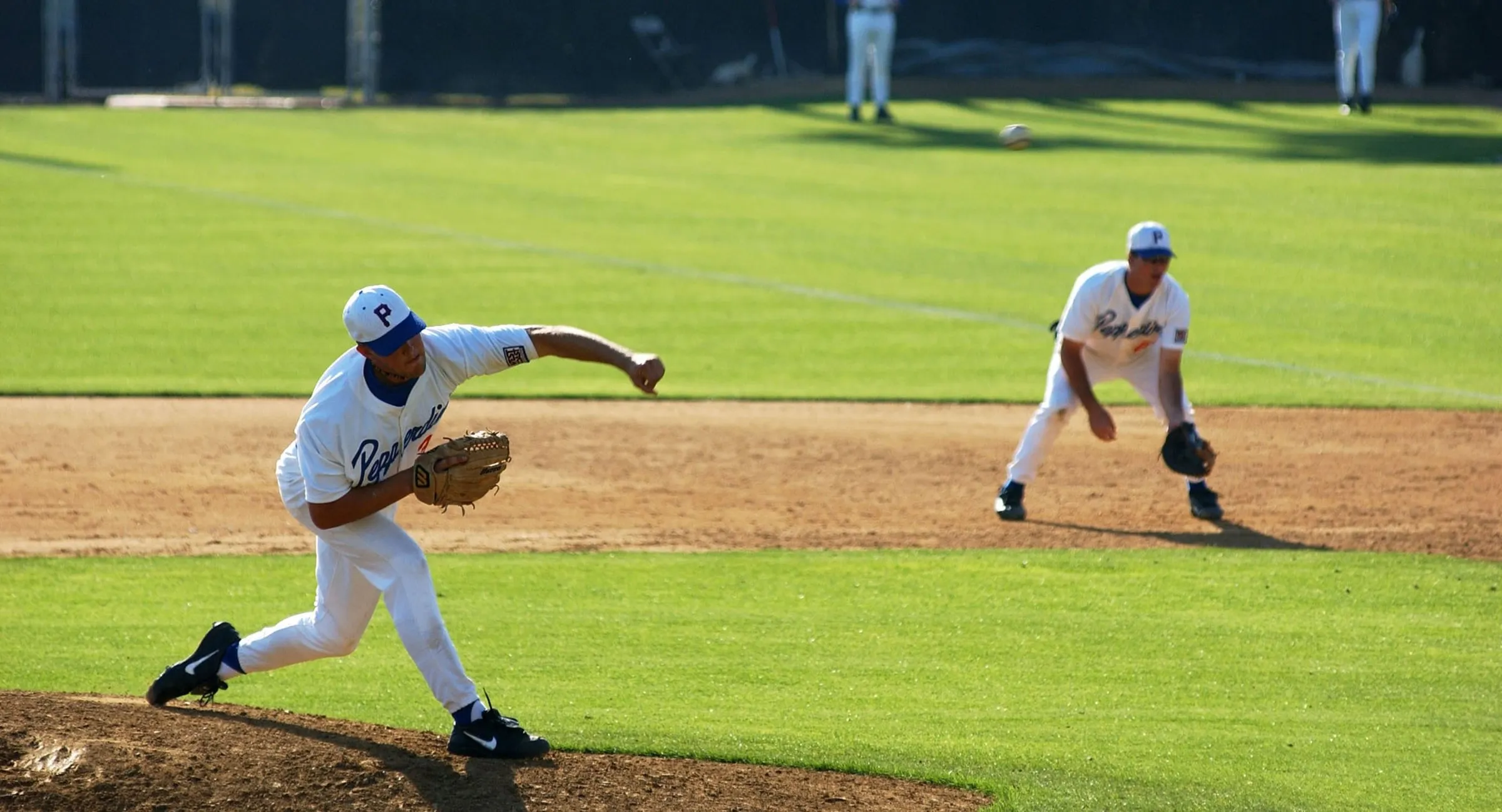 A Pepperdine pitcher delivering a pitch with an infielder ready behind him